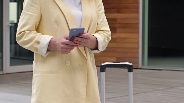 Business Woman with a Suitcase Uses a Mobile Phone and is Waiting for Someone