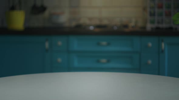 Female Hand Putting Yellow Flowers in Pot on the Table in Blue Kitchen