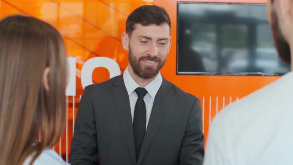 Salesman Transmitting Keys To Young Couple in Car Dealership.