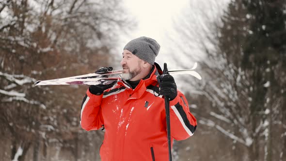 Sporty Mature Man with Skis Standing in Forest in Winter