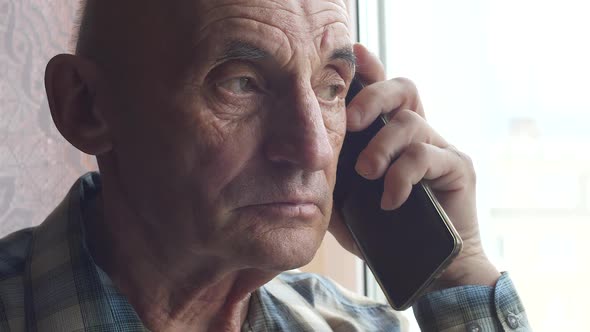 Portrait of a serious caucasian pensioner 70 years old listening attentively holding a smartphone. S