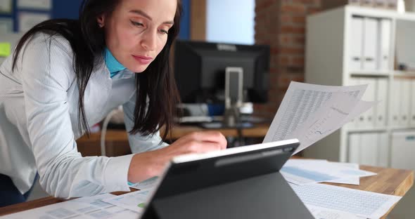 Woman Looking Into Digital Tablet with Documents with Charts in Hands in Office Late at Night Movie