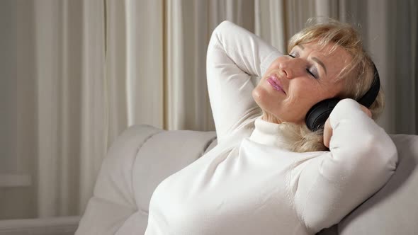Blonde Woman of Middle Age Listens to Music Via Headphones