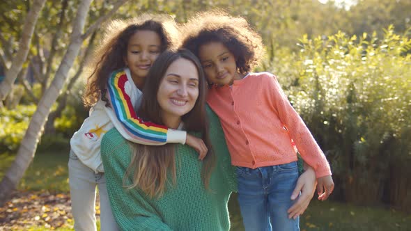 Caucasian Young Mom and Afro Daughters Hugging in Park