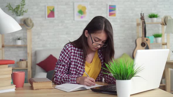 Beautiful Asian Girl in the Living Room at Homesitting at the Table with a Laptop and Studying