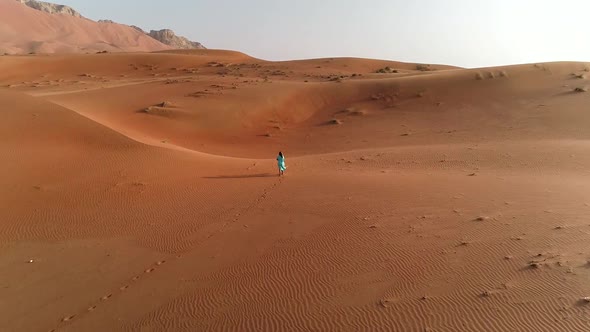 Aerial view of woman walking and making photo in desert, Dubai, UAE.