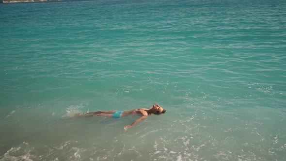 Relaxed Handsome Athletic Man in Blue Swim Trunks Enjoying By Lying on Turquoise Water of