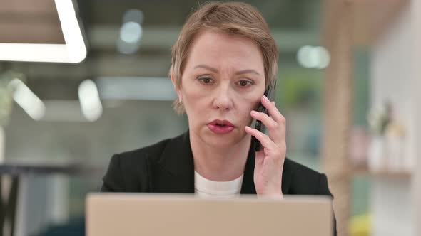 Close Up of Old Businesswoman with Laptop Talking on Smartphone 