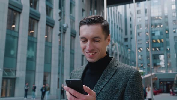 Successful Happy Businessman Texting Messages on His Smartphone. Young Man Is Standing in Business