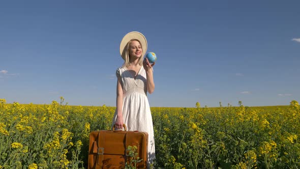 Blonde woman in white dress with suitcase in rapeseed field in spring time