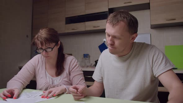 Family sitting at home looking through receipts of purchases, a man is dissatisfied with spending