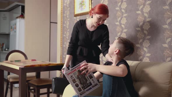 Mother with Red Hair Talks to Young Son Reading Book on Sofa
