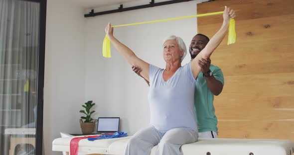 Video of happy caucasian senior woman exercising with african american male physiotherapist