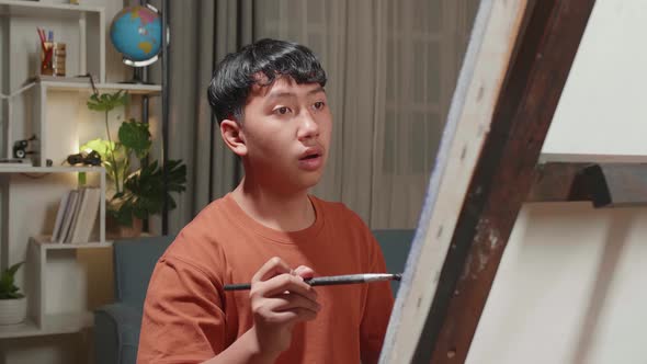 Asian Artist Boy Holding Paintbrush Mixed Colour And Thinking Before Painting On The Canvas