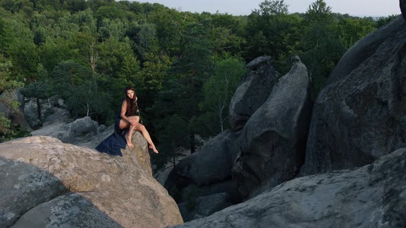 Wild Medieval Woman in Blue Dress Sits on Edge of Camus Rock and Strokes Herself