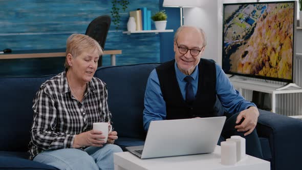 Enthusiastic Couple of Pensioners Sitting Together on Sofa Talking on Video Call