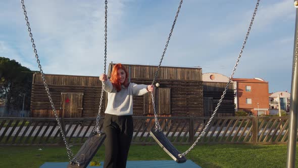 Young Beautiful Red Hair Girl Enjoys at the Park Playing with the Swing