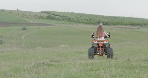 Free Woman Rides a Quad Near the Forest on a Plain of Green Grass