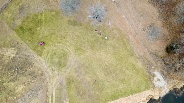 Birds eye view of four wheeler driving around large empty field by a lake. Drone shot from a birds e