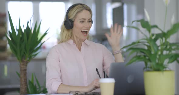 Blond woman with headphones making video call on laptop