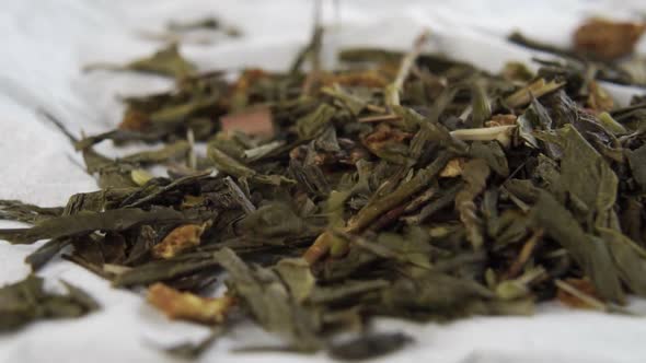 Dried green leaves of herbal hemp tea fall onto a white paper napkin