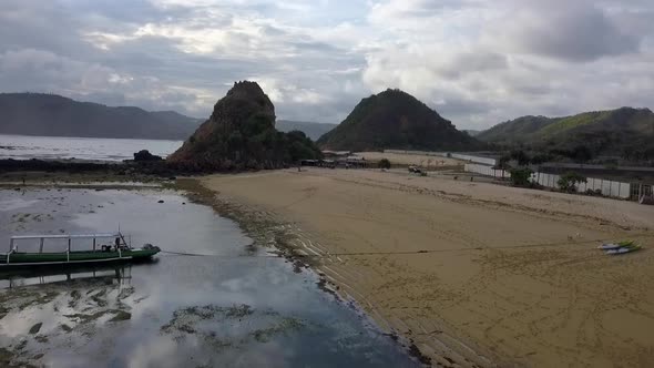 Small hill, surfboards on beach and a boat in water.Spectacular aerial view flight fly backwards dr