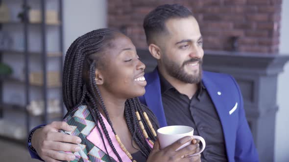 African American Woman and Caucasian Man Looking at the Window and Smiling. Happy Couple with a Cup