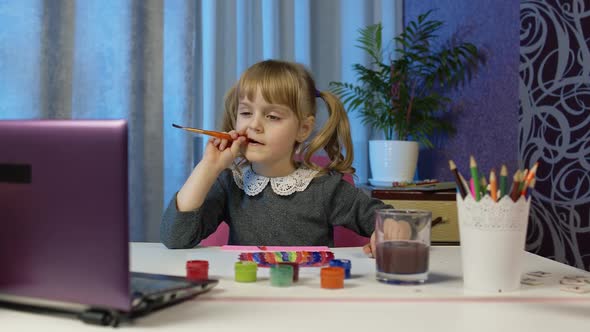 Girl Enthusiastically Drawing with Brushes and Paints Using Laptop at Home Distance Education