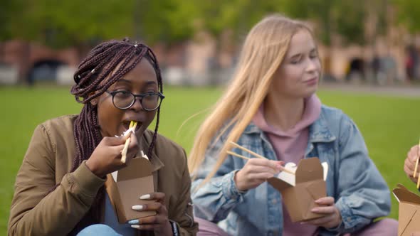 Close Up of Diverse Young Man and Women Sitting on Grass Eating Wok and Chatting