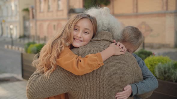 Happy Children Hugging Male Caucasian Retiree and Smiling at Camera. Portrait of Joyful