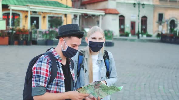 Two Tourists in Protective Masks Using Map on Central City Square
