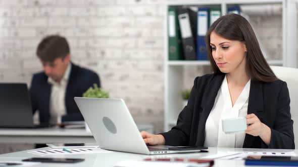 Focused Young Businesswoman Drinking Coffee or Tea at Workplace During Working Using Laptop