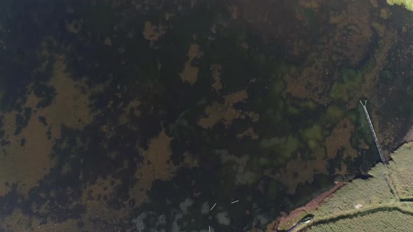 Aerial tracking forward topdown over a peninsula of land sticks out into a lagoon. A stone structure