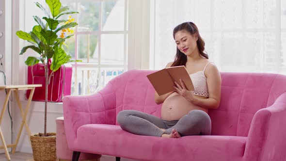 Happy Pregnant Woman sitting on couch holding book and reading for prepare to take care baby