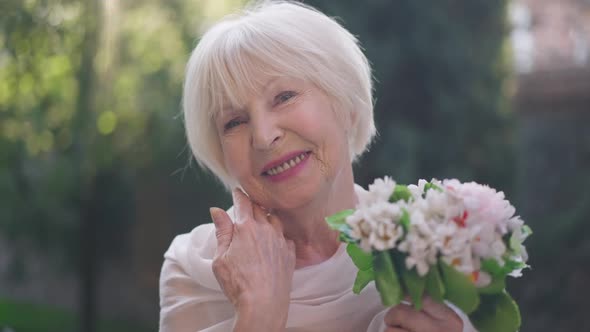 Beautiful Woman with Grey Hair Holding Bridal Bouquet Standing in Sunrays Outdoors