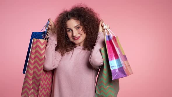 Happy Young Woman with Colorful Paper Bags After Shopping Isolated on Pink 