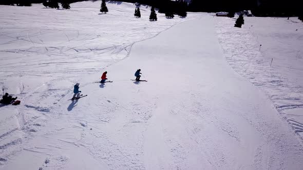 Aerial of ski resort at sun mountains with pine forest. Skiers ride down on snow slope at lifts. Win