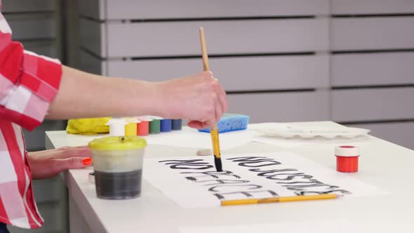 Close-up, Hand Writes Slogan with Brush, Using Black Watercolor Paint on White Banner, Poster