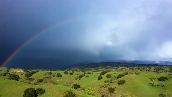 Farmland hills with cattle with beautiful double rainbow and mountains with snow and storm weather d