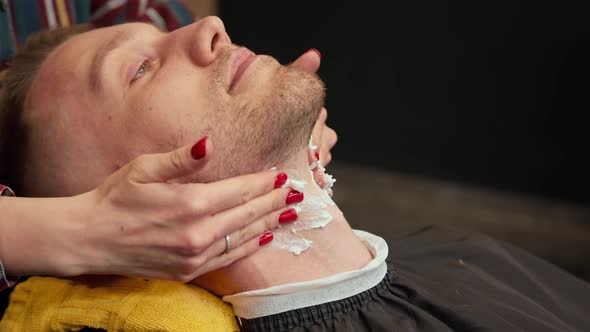 Barbershop: female hairdresser uses beard cream while trimming beard