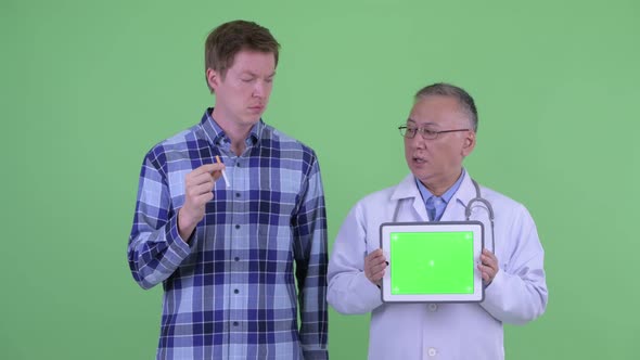 Mature Japanese Man Doctor with Young Man Explaining Effects of Smoking