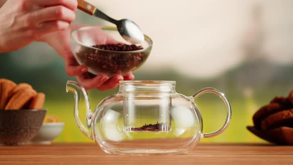 Putting Dry Tea Leaves Into Teapot on a Wooden Table