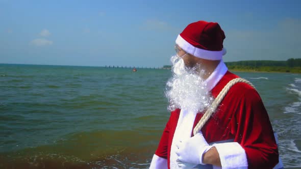 Santa Claus in suit walks along seashore with bag on his shoulder.