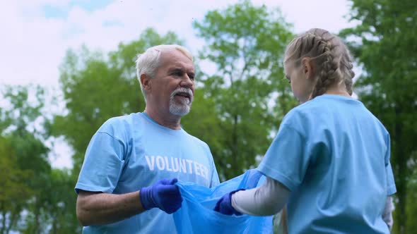 Smiling Elderly Volunteer With Granddaughter Collecting Garbage Giving High Five