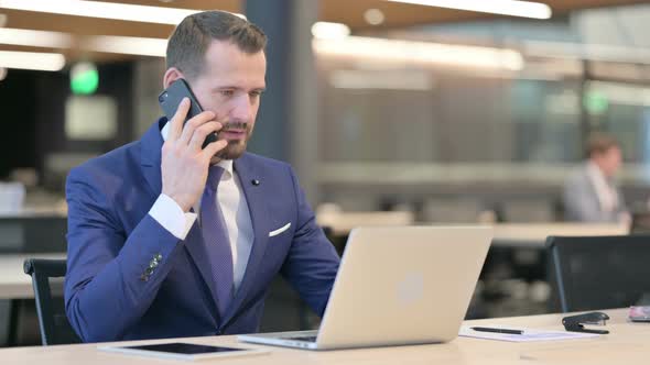 Middle Aged Businessman with Laptop Talking on Smartphone