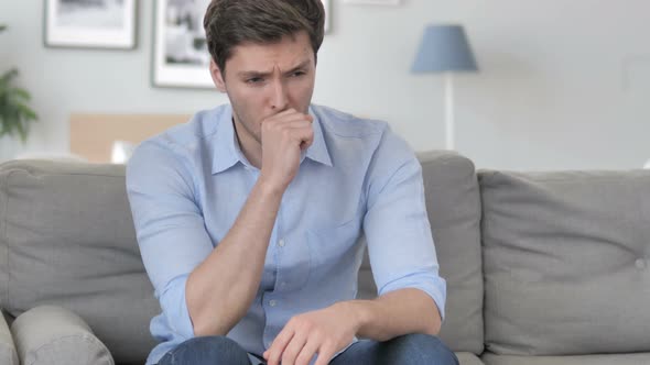 Young Man Coughing while Sitting on Couch