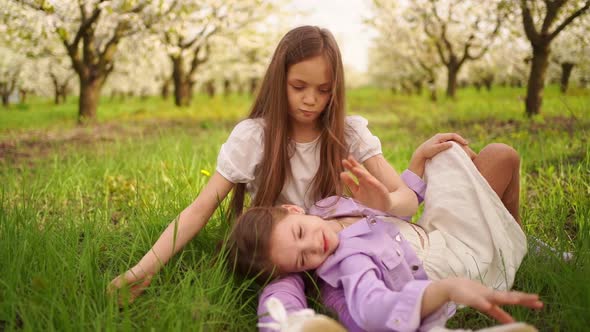 Two Longhaired Girls Sisters on the Lawn in the Garden with Flowering Trees