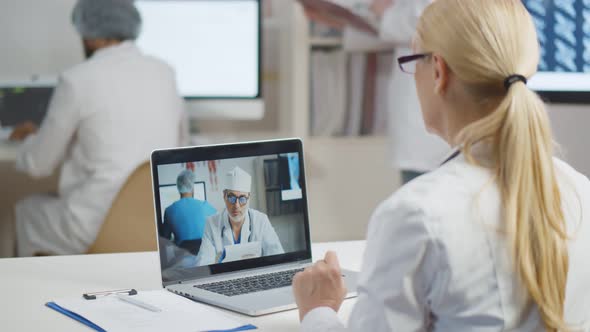Back View of Woman Doctor Consulting Colleague Via Video Conference on Laptop
