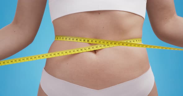 Close Up Shot of Woman Measuring Her Waist with Measure Tape Blue Studio Background