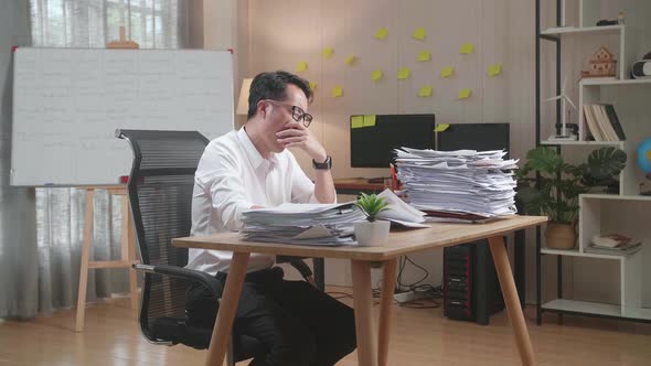 Tired Asian Man Yawning And Taking Off His Glasses Before Sleeping While Working Hard With Documents